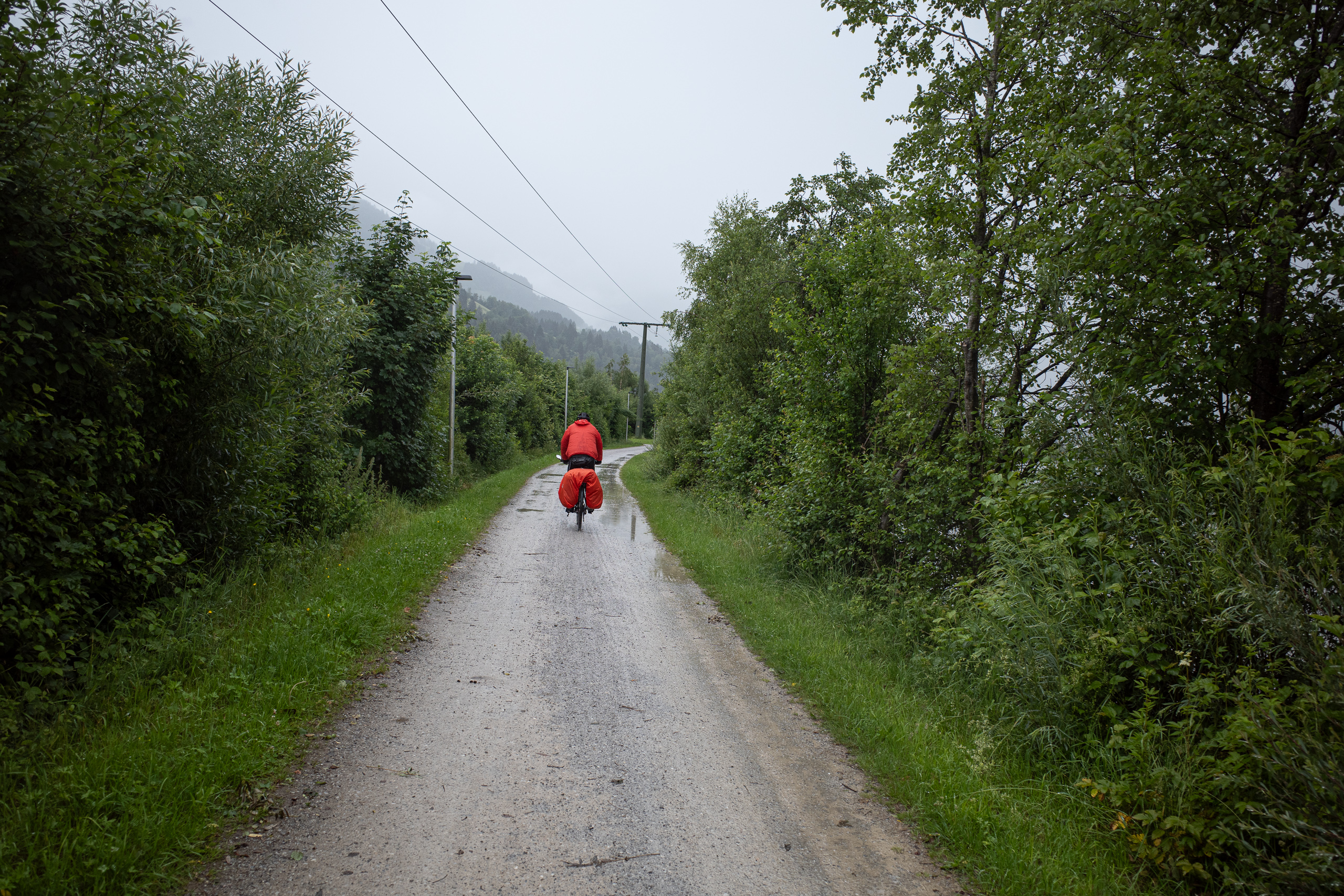 Weiter hinein in den Regen: rote Jacke, graue Wolken über dem Tal